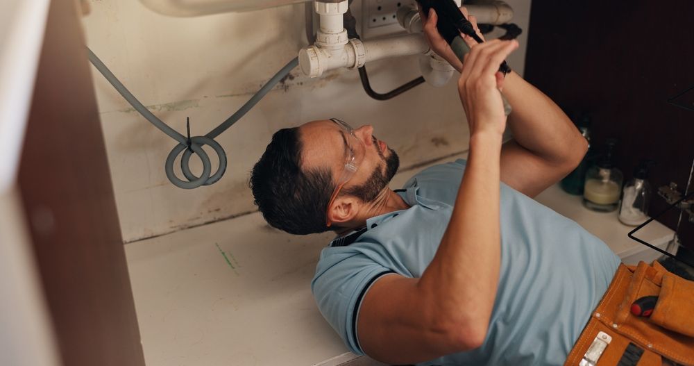 Plumber lying on a floor, working on pipes under a sink with tools nearby.