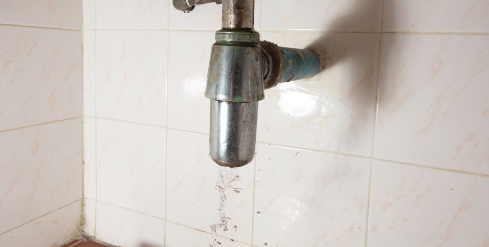 Leaking metal sink drain pipe against white tiled wall