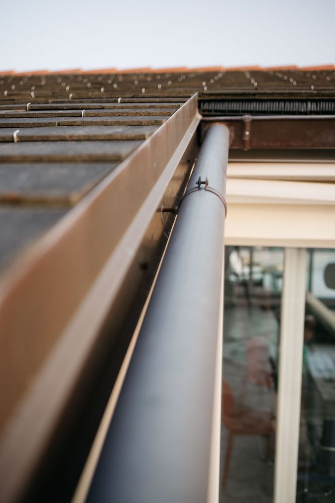 Close-up of a gray downspout beside a brick wall and roofline