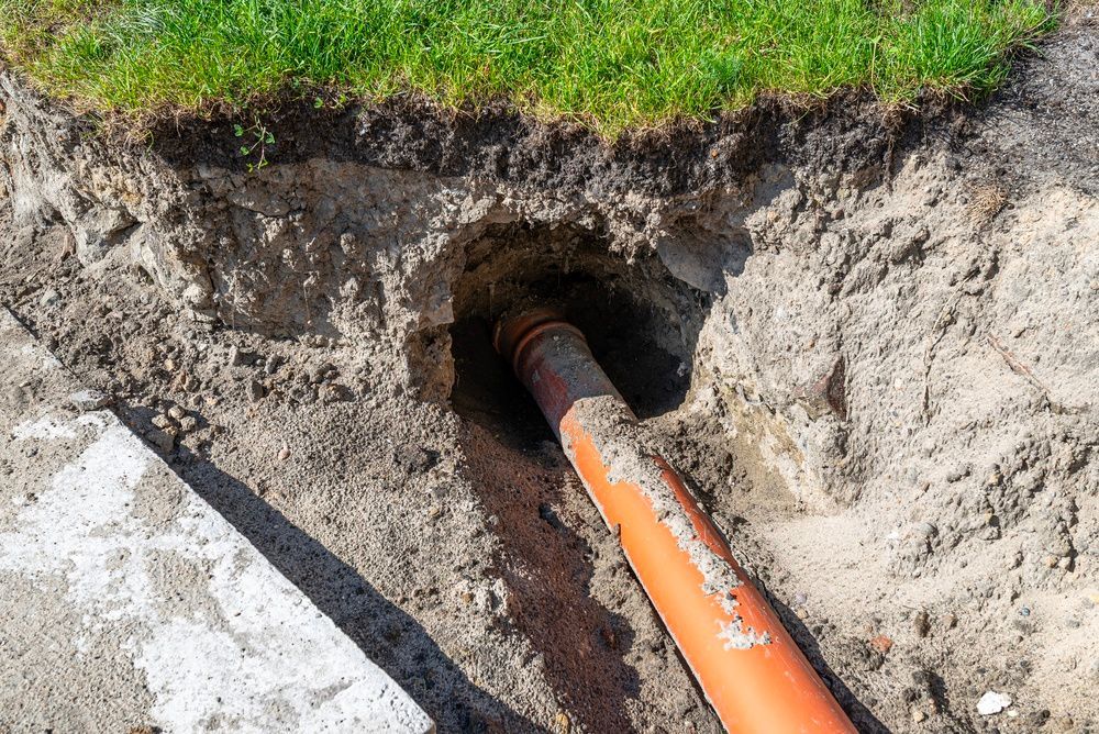 Orange utility pipe running through a dug trench under grass and soil