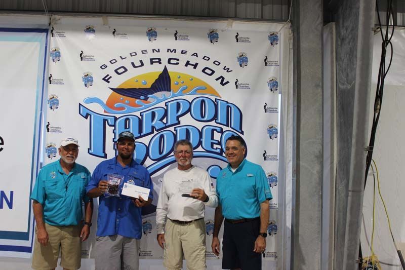 A group of men are standing in front of a tarpon rodeo banner.