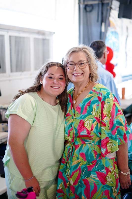 Two smiling people posing together indoors, one in a neon green shirt and one in a colorful tropical shirt.