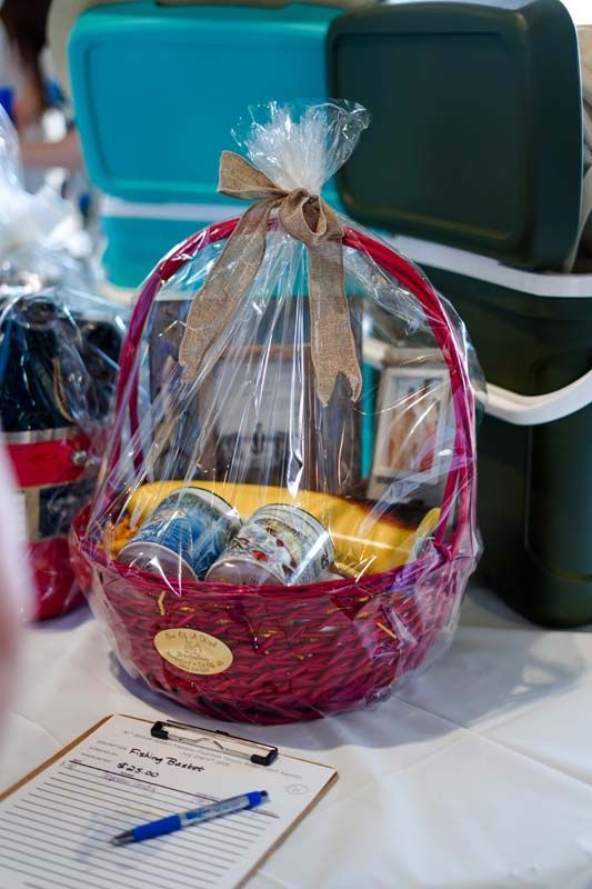 Gift basket with fruit and packaged snacks wrapped in clear cellophane, sitting on a table with a pen and paper.