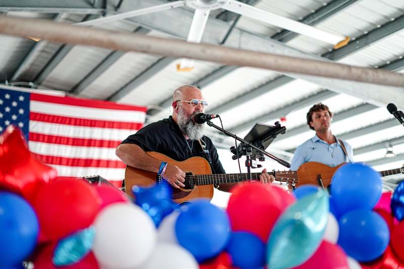 Musicians performing on stage with guitars, microphones, and red and blue balloons in front of an American flag
