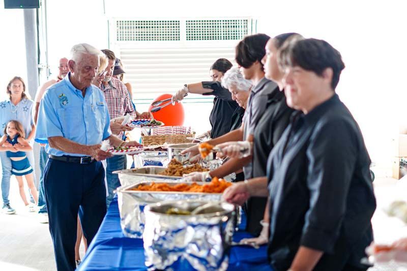People serving food at a buffet table in a bright dining hall