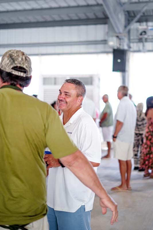 People chatting in a bright indoor hall, with one smiling man in a white shirt in the foreground