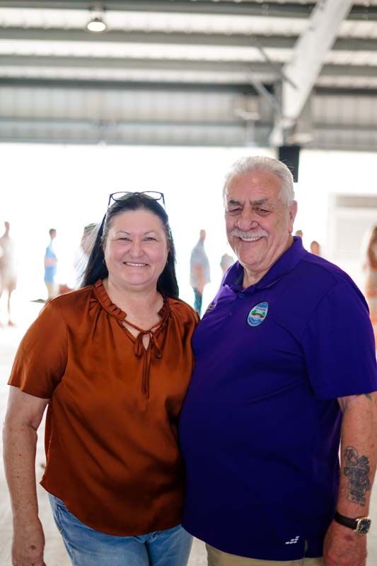 Two smiling people standing together in a bright indoor space, wearing orange and purple shirts.