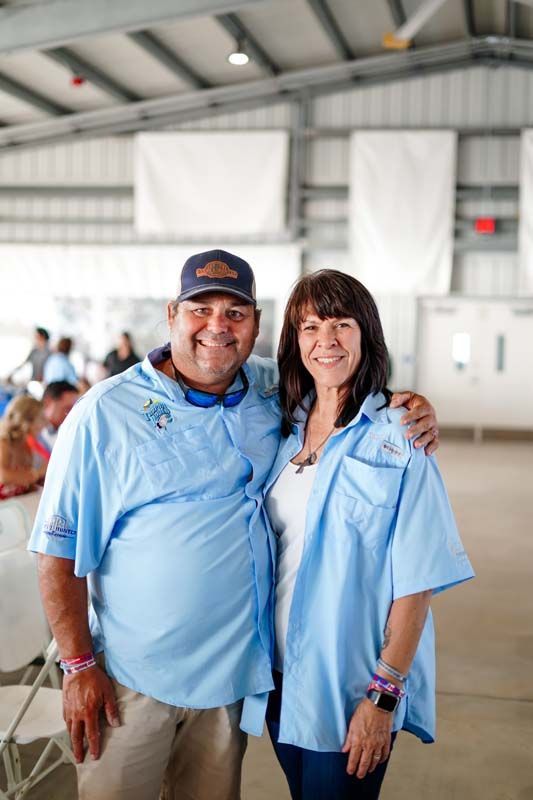Two people in matching light blue shirts smiling together in an indoor hall