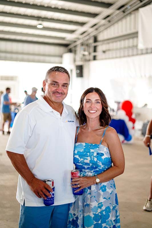 Two people smiling and posing indoors, holding drinks at a casual event.