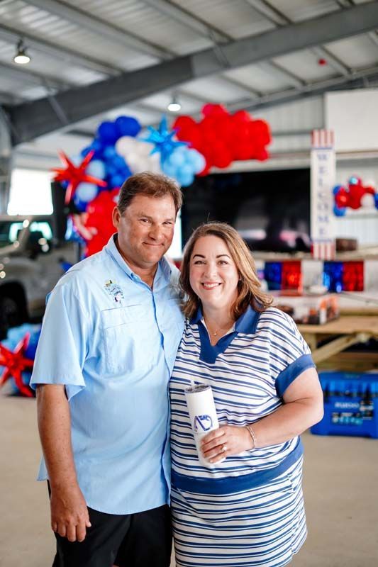 Two people smiling indoors at a red-and-blue balloon-decorated event, holding drinks.