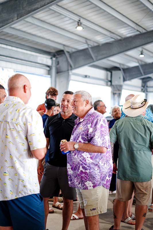 People chatting in a covered pavilion, with a man in a purple floral shirt in the foreground.