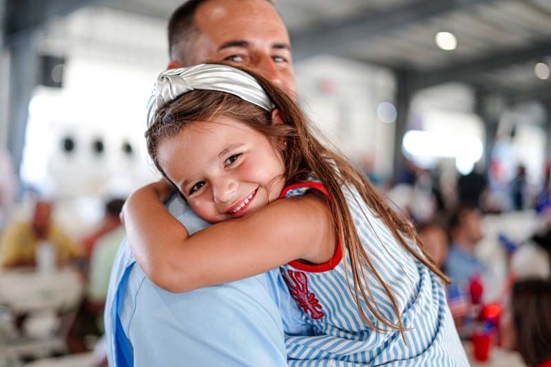 Smiling child in blue dress hugging an adult in a bright indoor setting