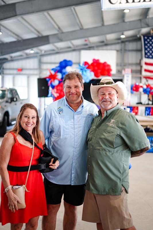 Three people posing indoors, with red, white, and blue balloons in the background.