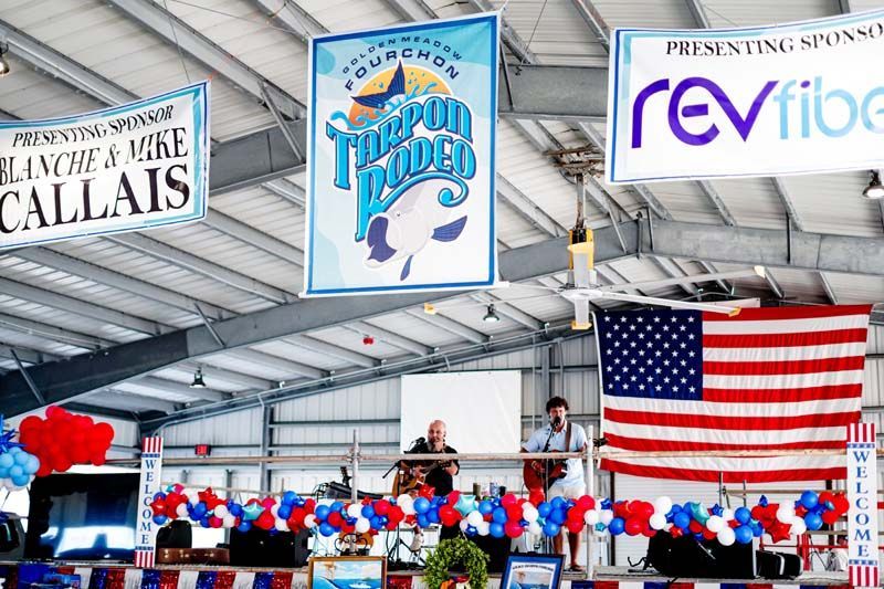 Speaker at a patriotic rally beneath banners and a large American flag, with red, white, and blue decorations