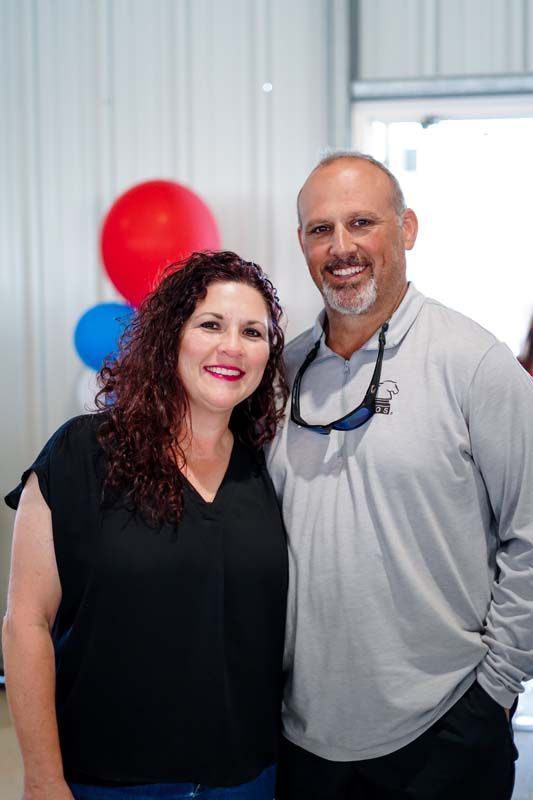 Two people smiling indoors with red and blue balloons in the background