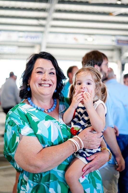 Woman holding a child, both smiling in a bright indoor setting.