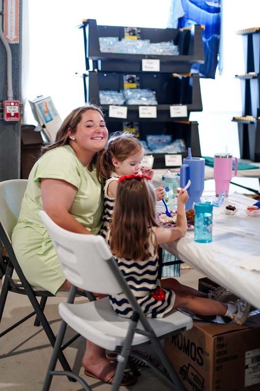 Woman and child sitting at a table in a storage room, smiling beside craft supplies.