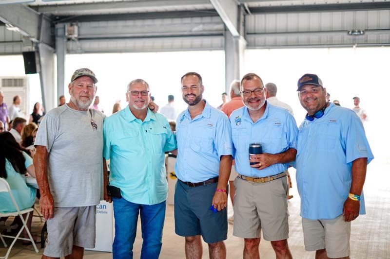 Five men in casual shirts stand together indoors, smiling and holding drinks at a social gathering.