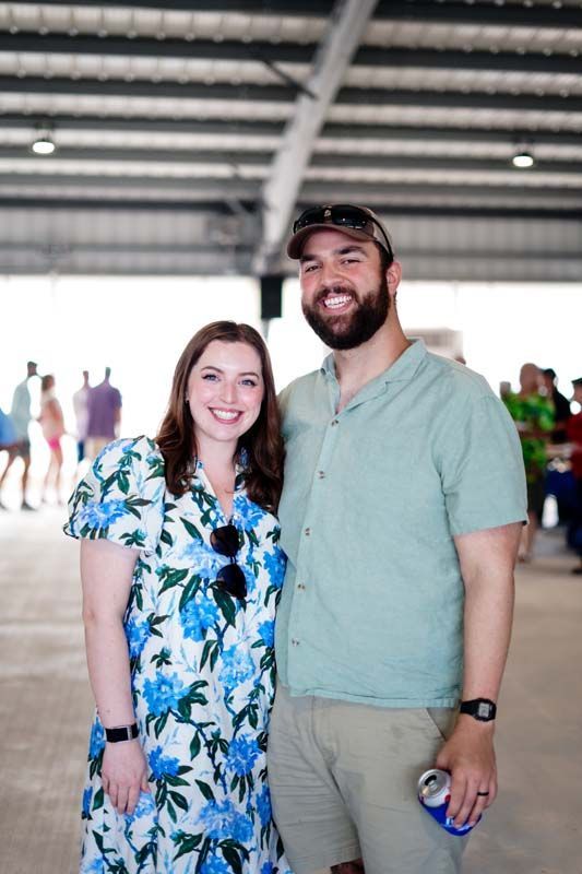 Smiling couple standing together in a large indoor venue, with people blurred in the background.