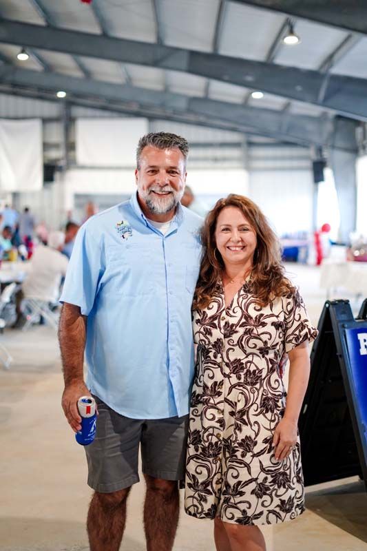Two people smiling in a warehouse-like venue, one holding a blue drink cup.