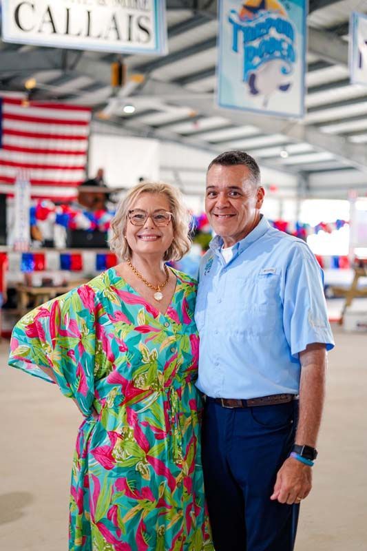 Two smiling people standing indoors under a Calais sign, with American flags in the background.