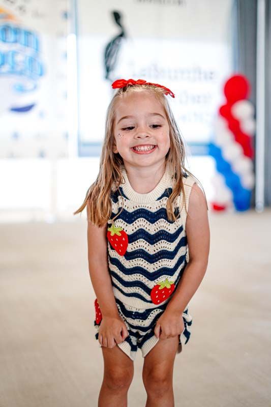 Smiling child in a blue zigzag dress at a festive party with red, white, and blue decorations