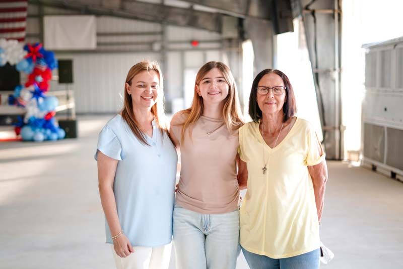 Three women standing together in a bright indoor space, smiling at the camera.