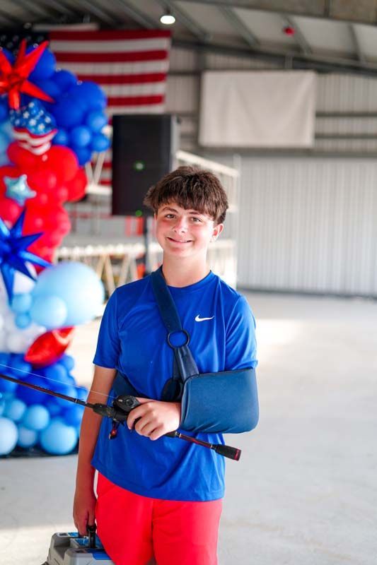 Person in a blue shirt and red shorts holding a fishing rod indoors beside a patriotic balloon display