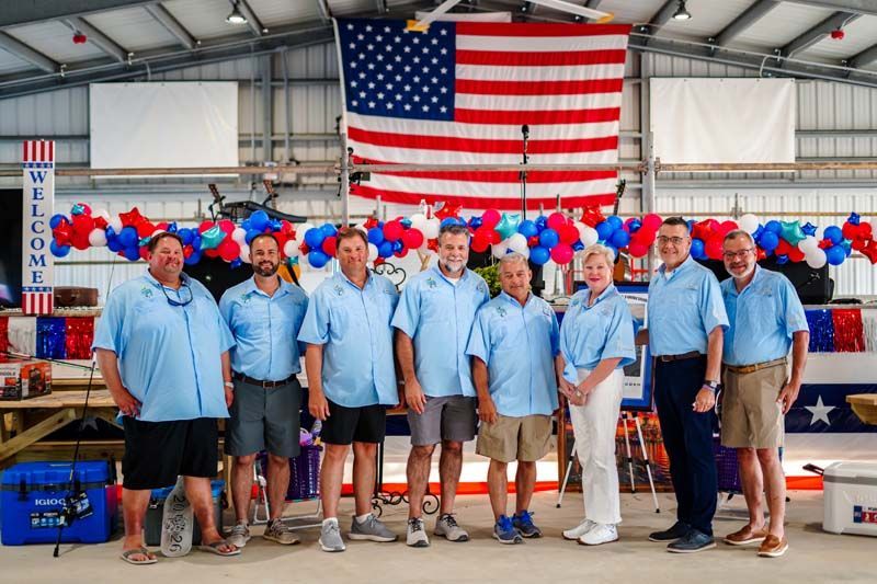Group of people in blue shirts standing under a large American flag at a decorated indoor event