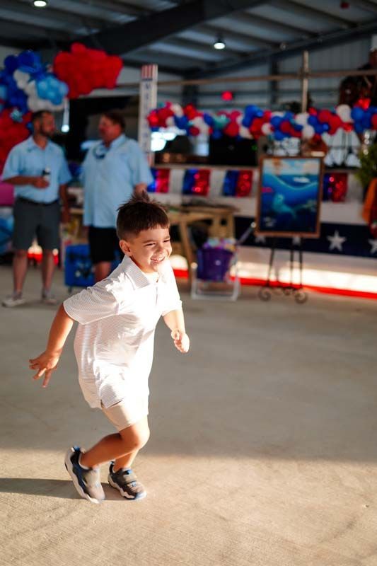 Child in white outfit running indoors at a festive event with red, white, and blue decorations