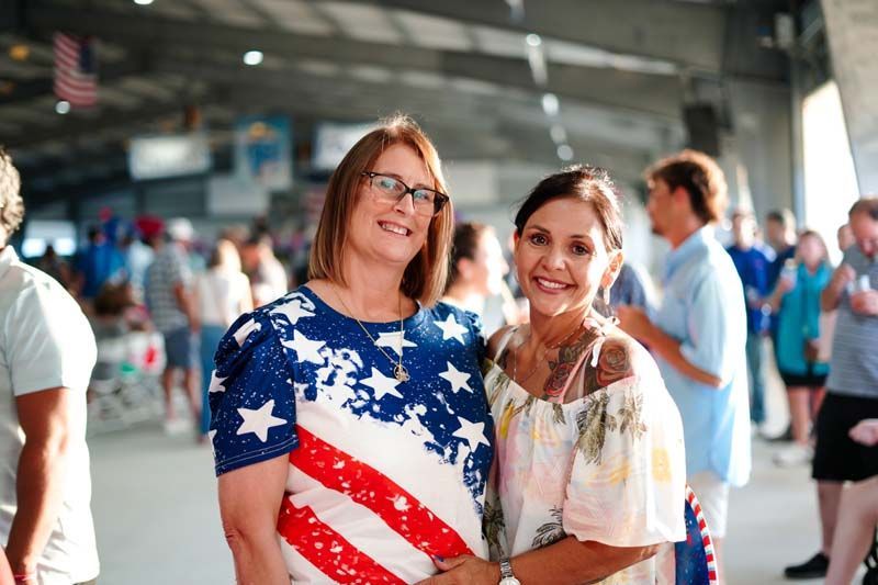 Two smiling people in patriotic shirts pose in a crowded indoor venue