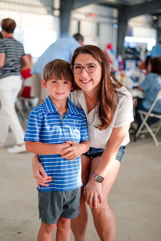 Woman crouching beside a smiling boy in a blue striped shirt in a bright indoor event space