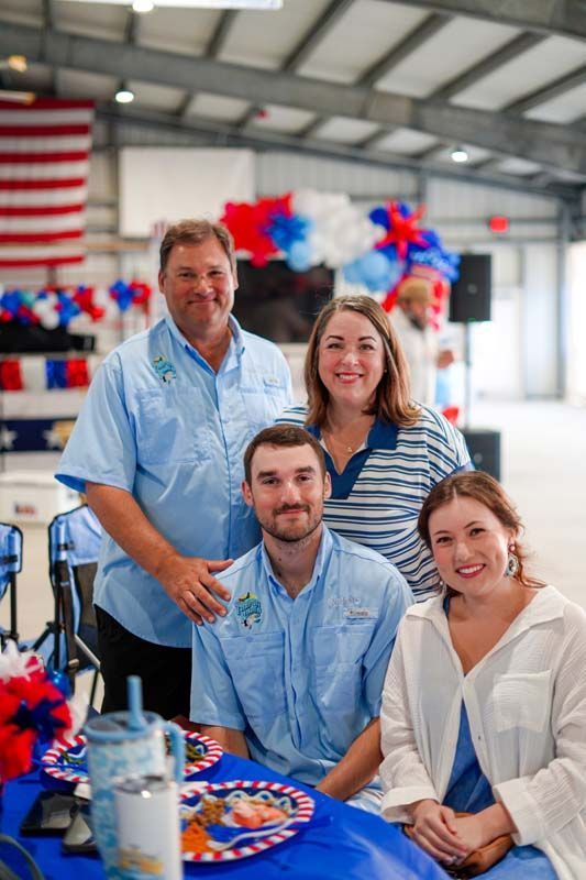 Four people posing at a red, white, and blue decorated event table inside a large hall