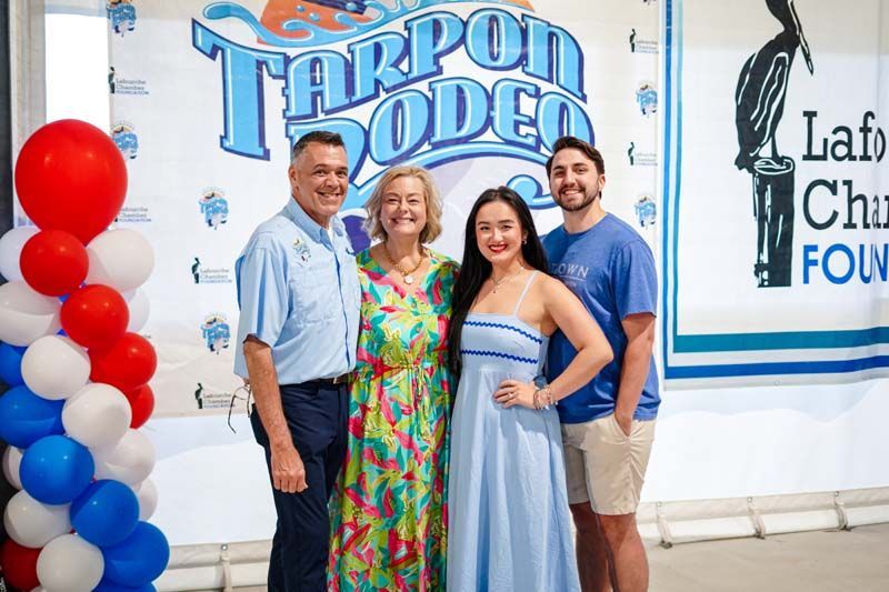 Four smiling people pose in front of a Tarpon Rodeo and foundation banner with red balloons.