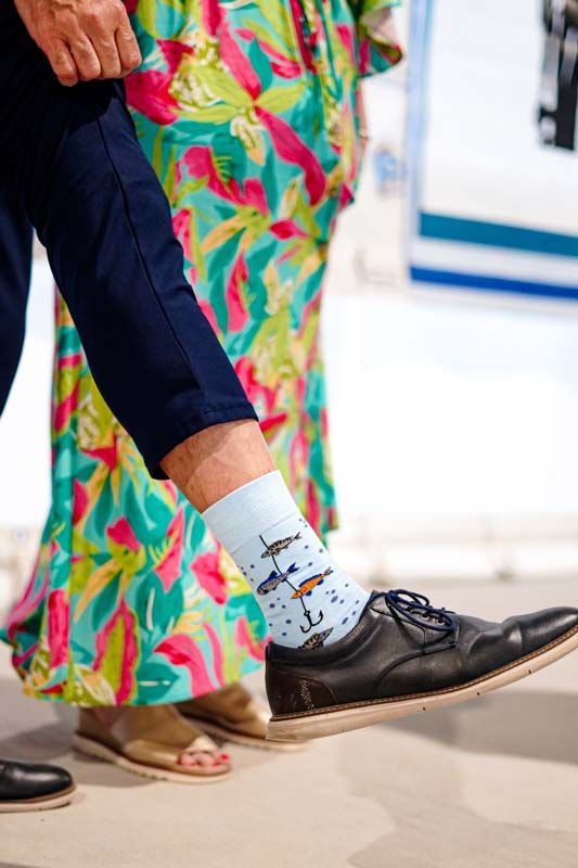 Black dress shoe and patterned sock beside a colorful floral skirt on a bright indoor floor