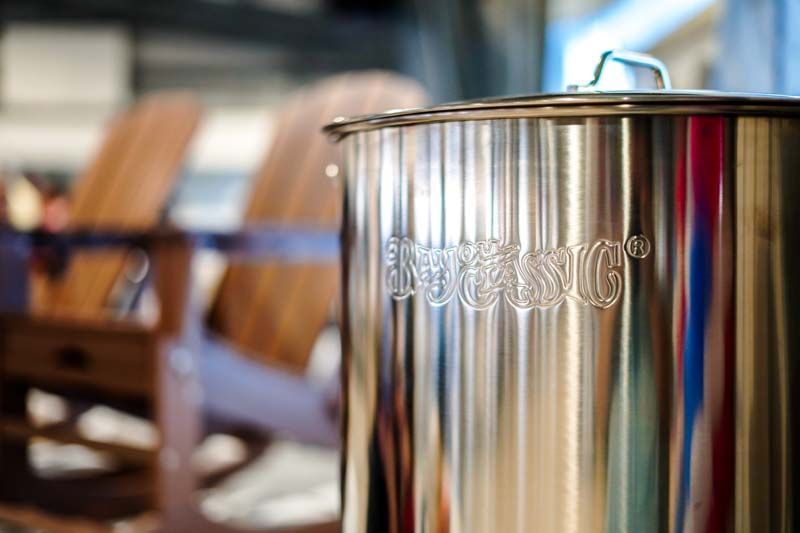 Stainless steel tank in a brewery, with rows of wooden barrels blurred in the background