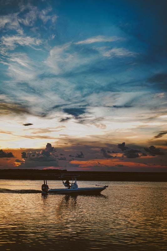 Boat with two people on calm water at sunset, silhouetted against a colorful sky.
