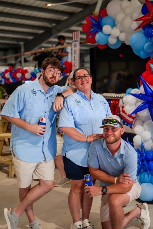 Three friends posing at a festive event with red, white, and blue balloon decorations