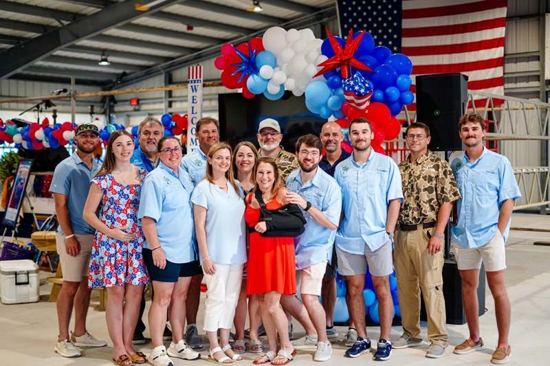 Group posing in front of red, white, and blue balloons and an American flag at a festive indoor event