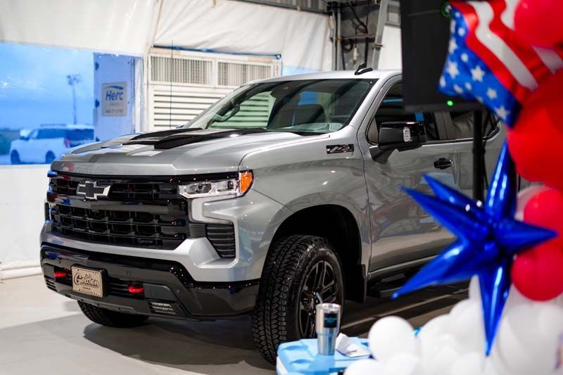 Silver pickup truck on display at an indoor event, with red and blue star-shaped balloons in front