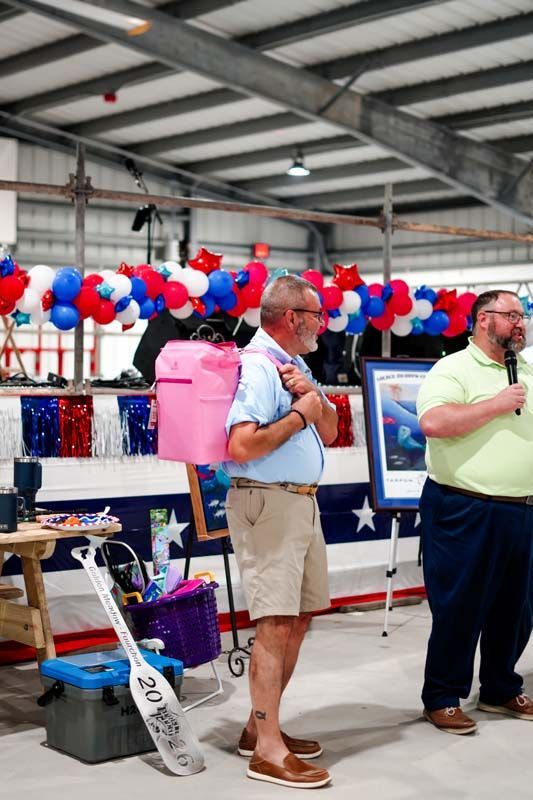 Two men speaking at a patriotic indoor event with red, white, and blue decorations and balloons