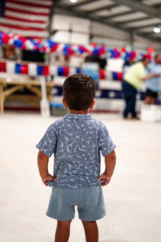 Child standing in a decorated hall, facing a blurred person near red, white, and blue bunting