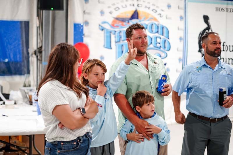 Four people at a trade show, one holding a product bottle and another holding a microphone, in front of a banner.