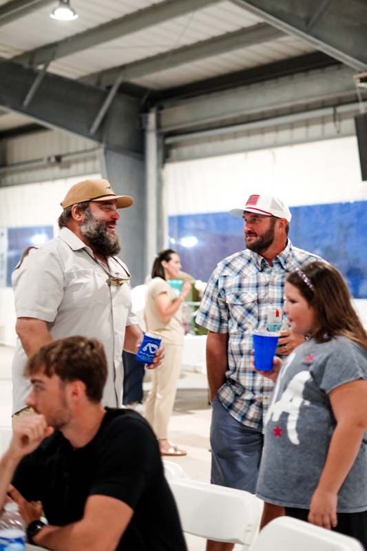 People chatting indoors at a casual event, holding blue cups in a warehouse-like space.