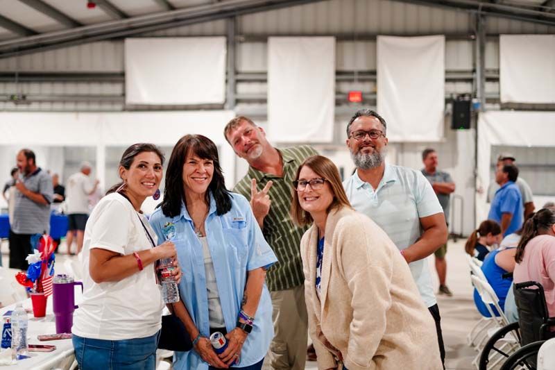 Five adults smiling at an indoor community event, standing together in a bright warehouse space.