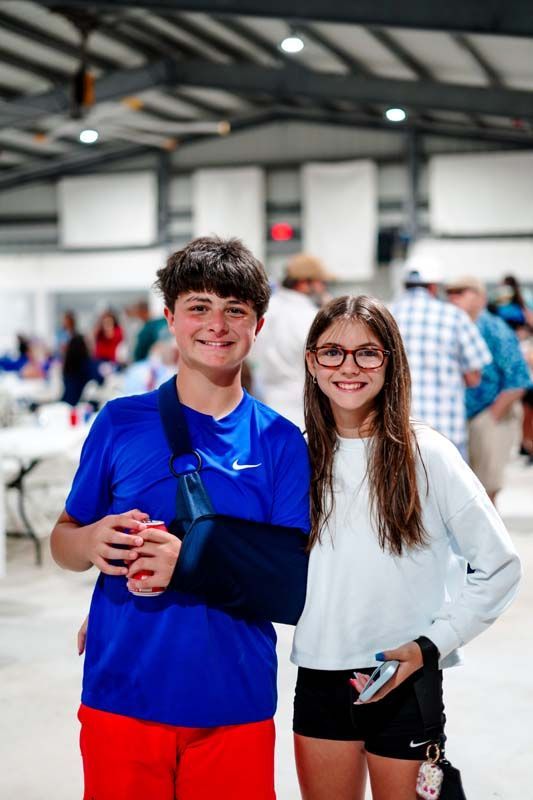 Two smiling teens in a gym, one in blue and red, the other in white and black, standing together.