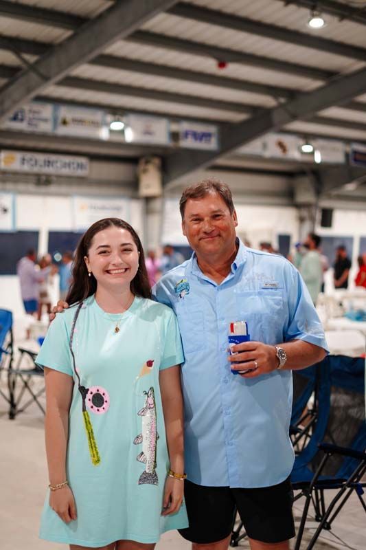 Two people posing in a large indoor hall, one holding a drink and both smiling.