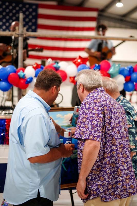 Two people talking in front of a ring with red, white, and blue balloons and an American flag backdrop