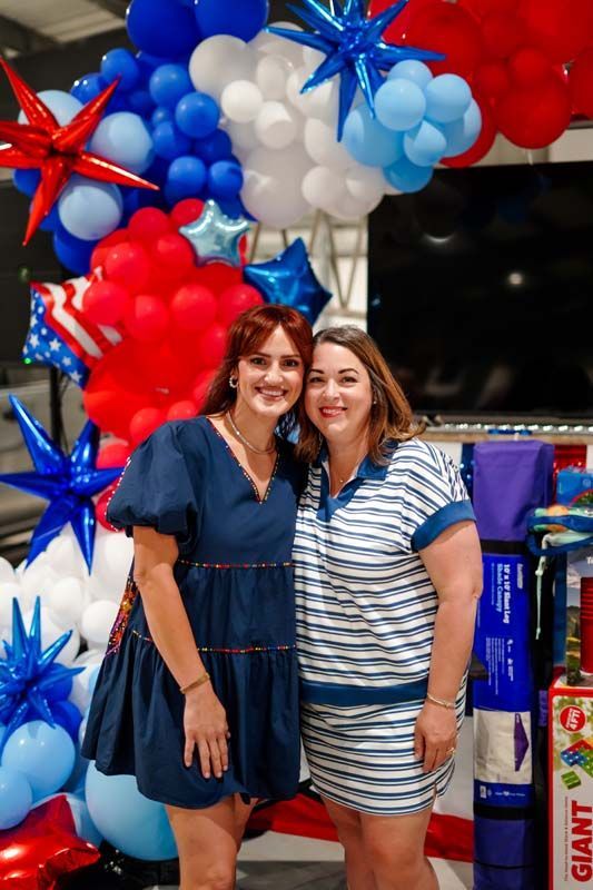 Two women smiling at a festive balloon display with red, white, and blue stars
