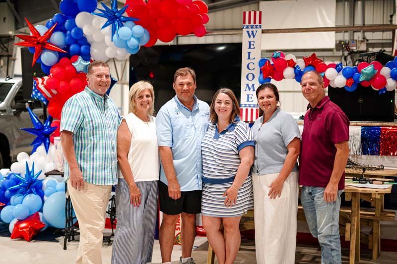 Five people posing indoors under red, white, and blue balloon decorations at an event booth